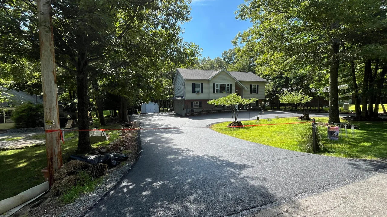 Freshly paved circular asphalt driveway through the trees to a raised ranch house, asphalt paving
