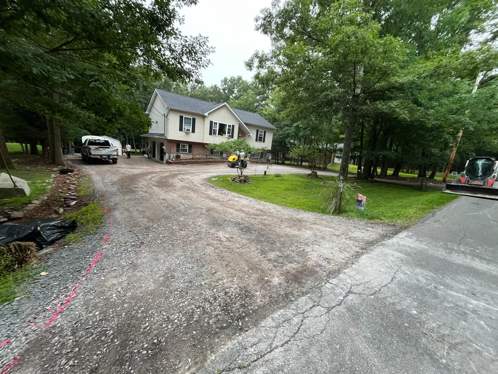 Driveway base being graded with a small roller and a compact track loader on site, asphalt paving