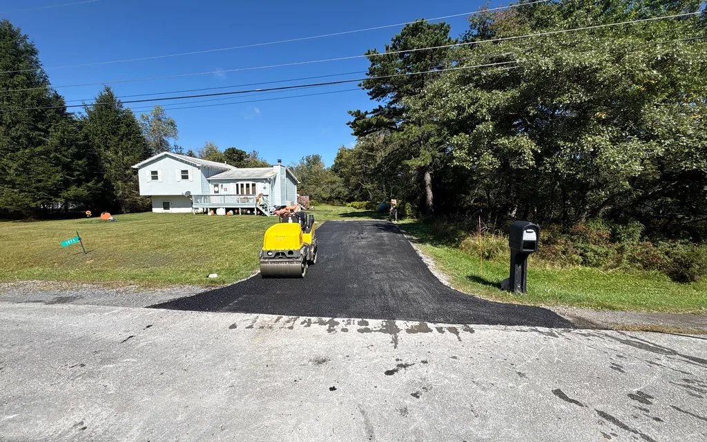 Small roller on a freshly paved asphalt driveway in front of a raised ranch house, asphalt driveway paving