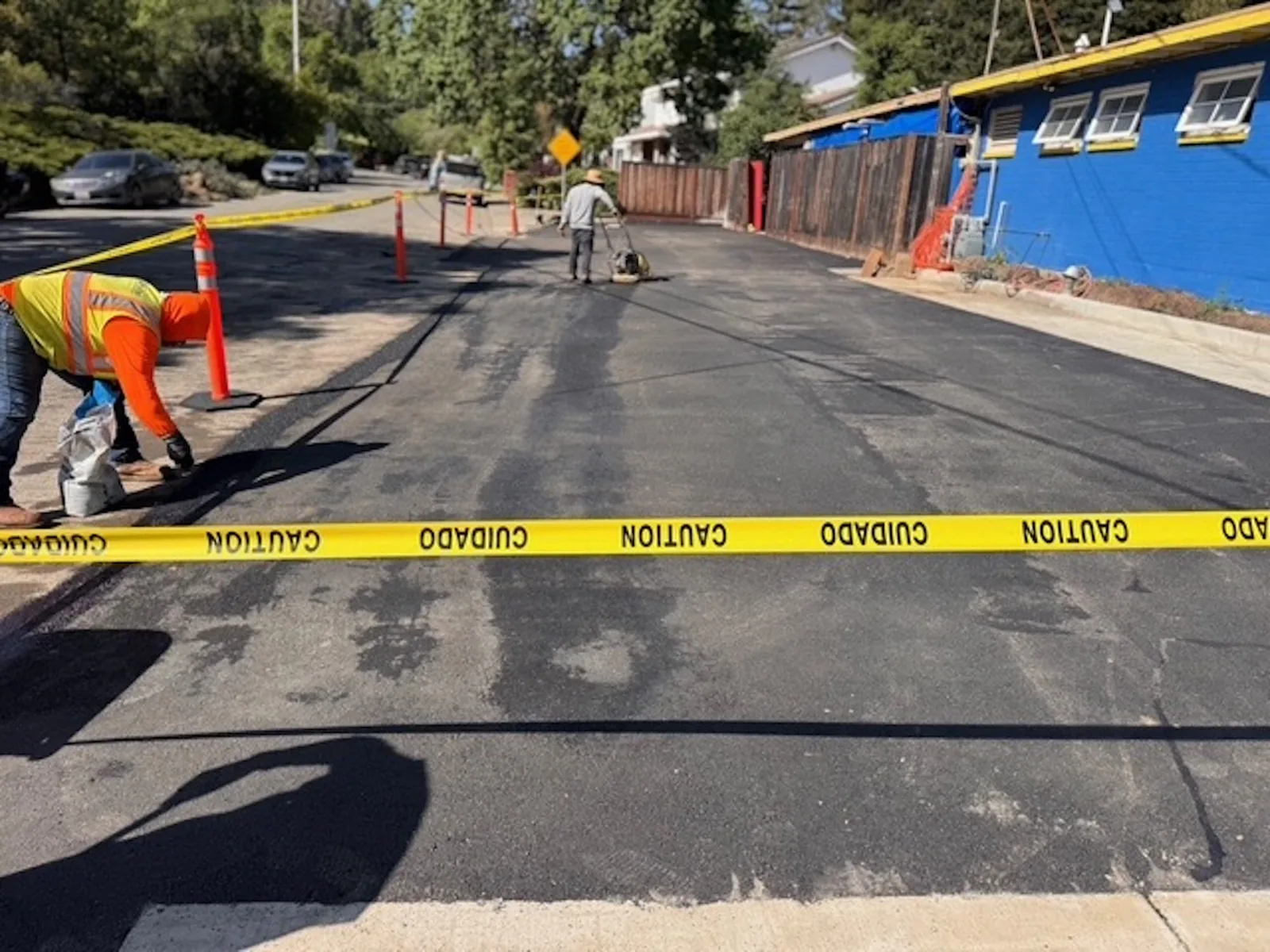 Crew running a plate compactor over fresh asphalt repair on a narrow lane, asphalt patching and repair