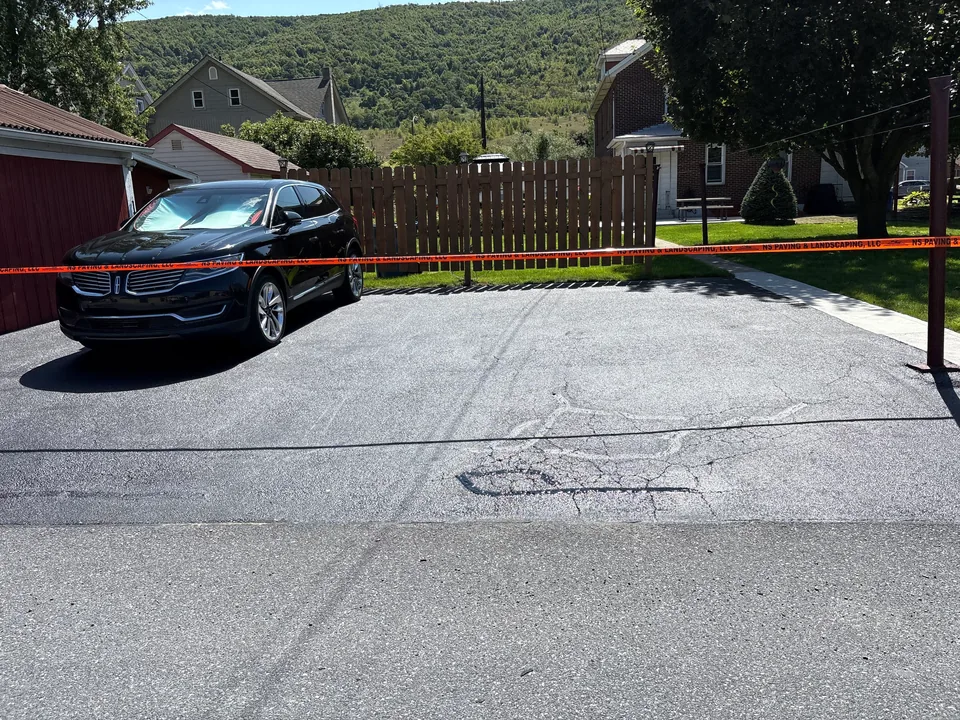 Sealed driveway showing an older patch outline and filled cracks, asphalt patching and repair