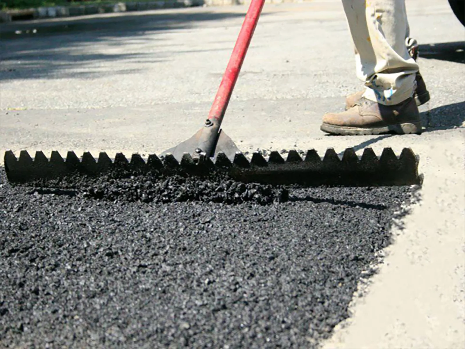 Lute rake spreading fresh hot asphalt into a pothole patch, asphalt patching and repair