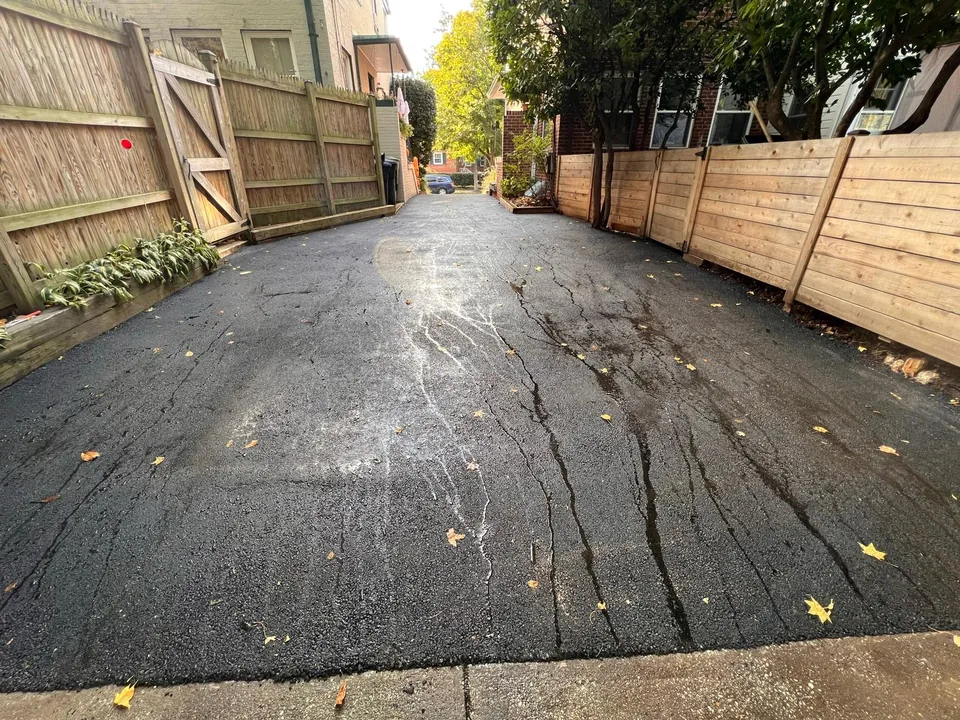 Fresh asphalt overlay on a narrow driveway between wood fences, asphalt resurfacing