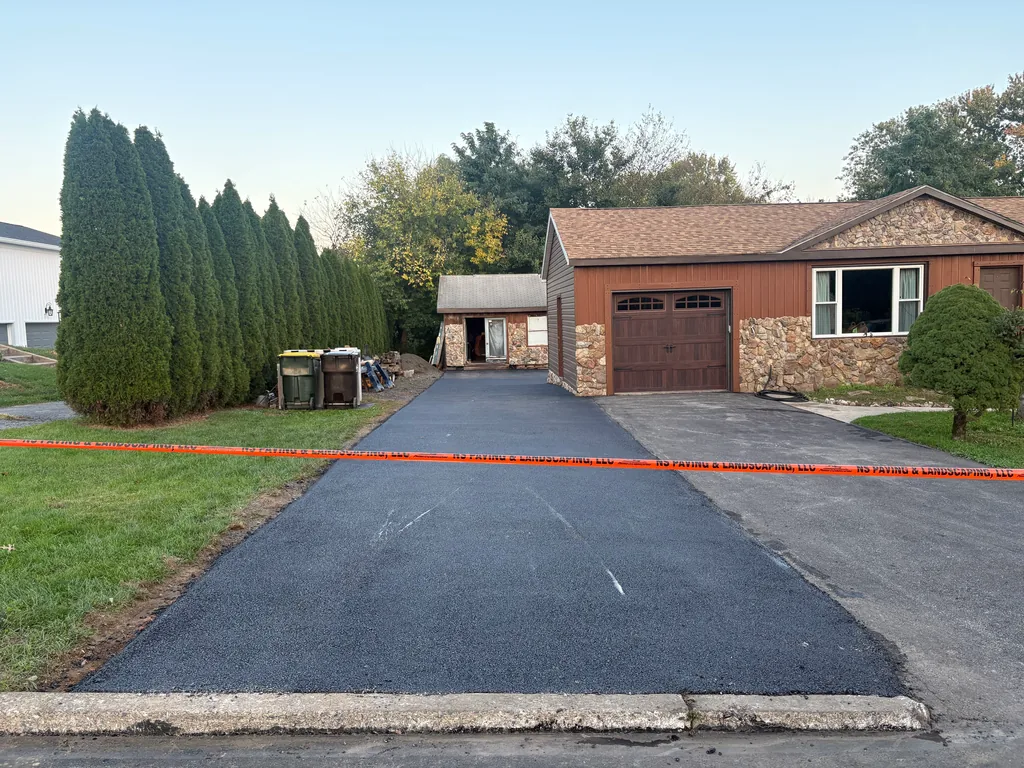 Fresh asphalt driveway lane beside older pavement in front of a ranch house garage, asphalt resurfacing