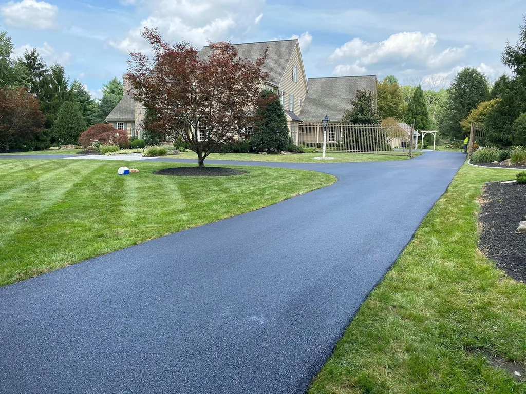 Long freshly surfaced asphalt driveway curving past a mowed lawn to a large house, asphalt resurfacing