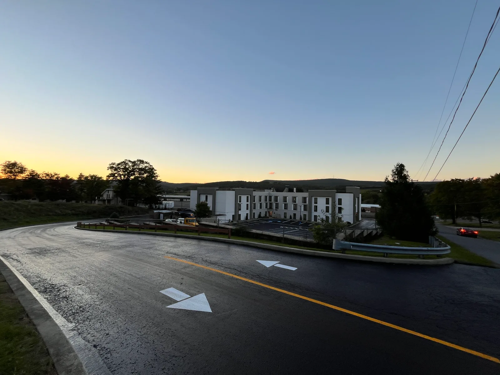 Sealed access drive with fresh arrows and a yellow center line at dusk, asphalt sealcoating
