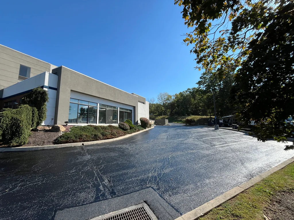 Glossy fresh sealcoat on a commercial lot along a building, asphalt sealcoating