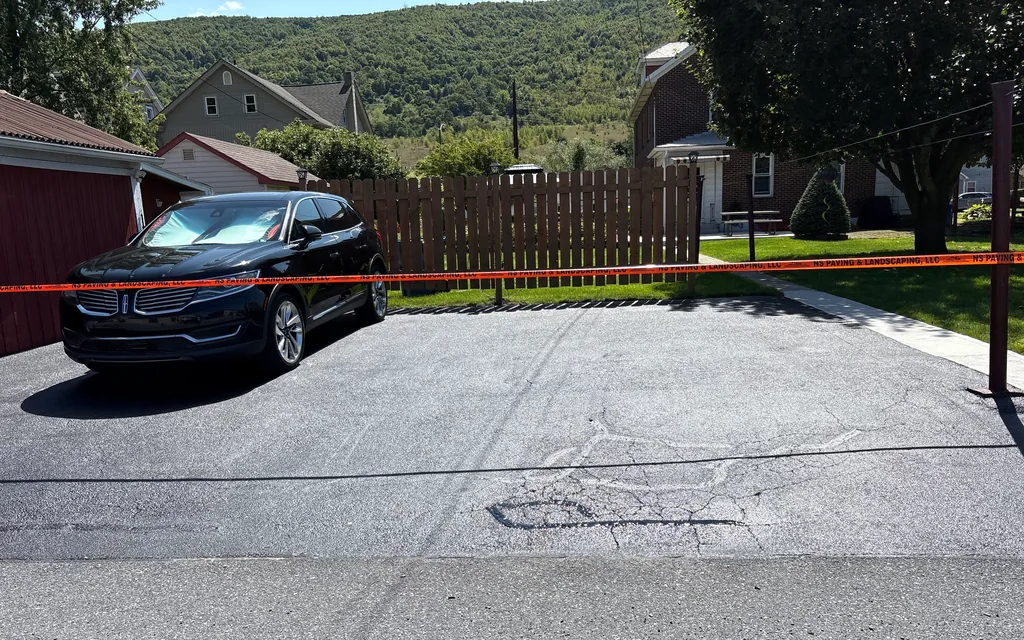 Sealed residential driveway taped off with older cracks showing through the coat, asphalt sealcoating