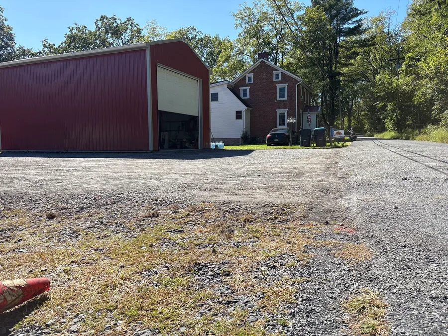 Graded stone yard in front of a red pole barn and a brick house, gravel driveway regrading