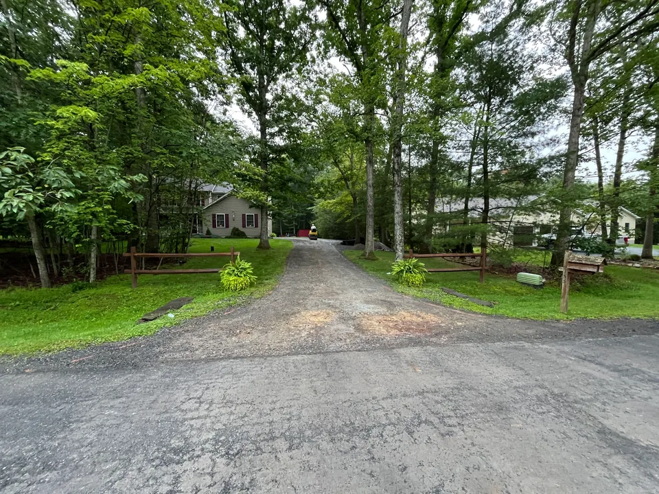 Graded stone driveway between split rail fences with a small roller at work, gravel driveway regrading