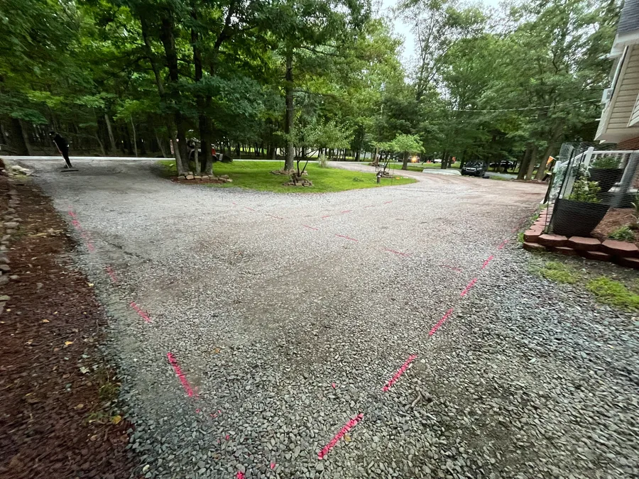 Graded stone driveway with pink layout marks under tall trees, gravel driveway regrading