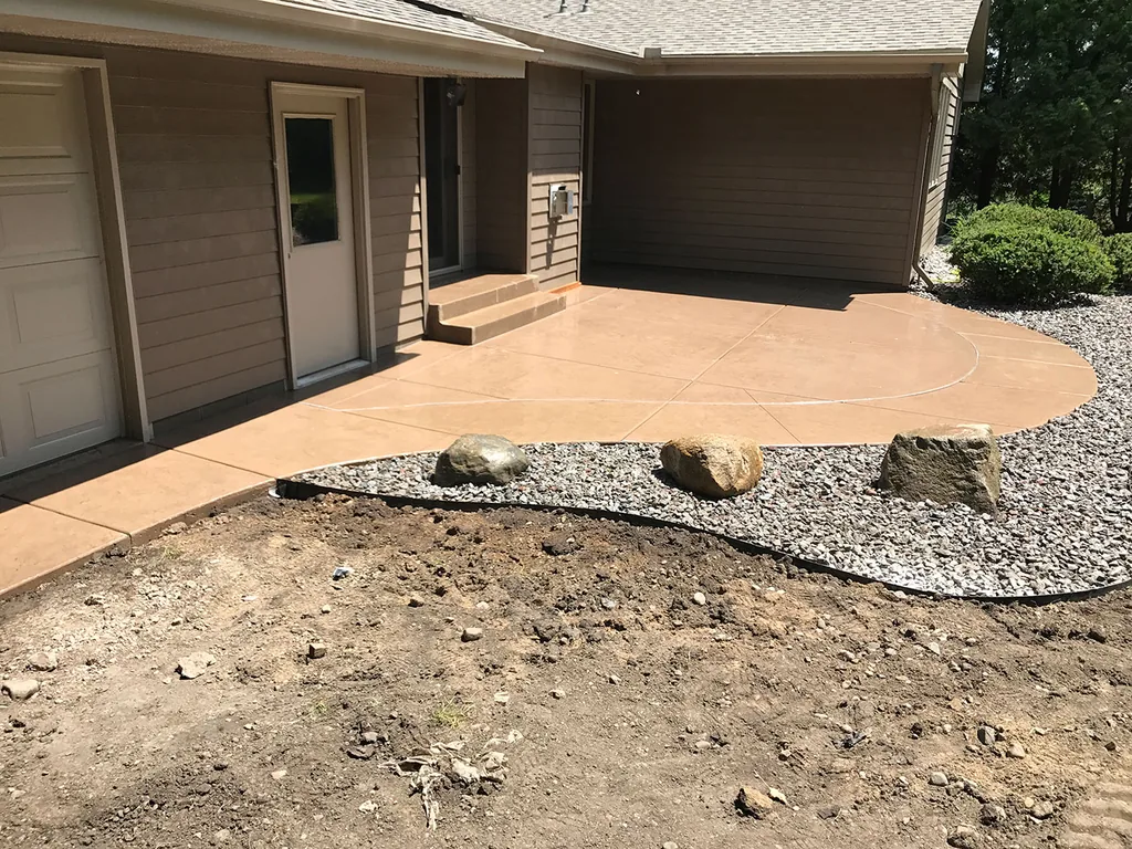 Colored concrete patio along a house wall with a river rock bed, hardscaping and patios
