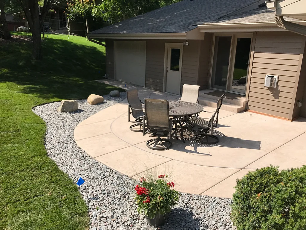 Tan colored concrete patio with a sawcut circle pattern beside a lawn, hardscaping and patios