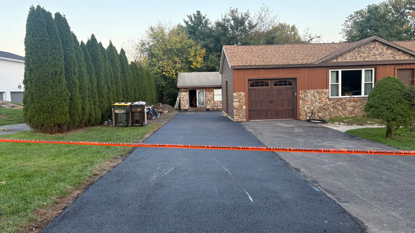 Freshly paved asphalt driveway taped off beside a stone front ranch house, asphalt paving