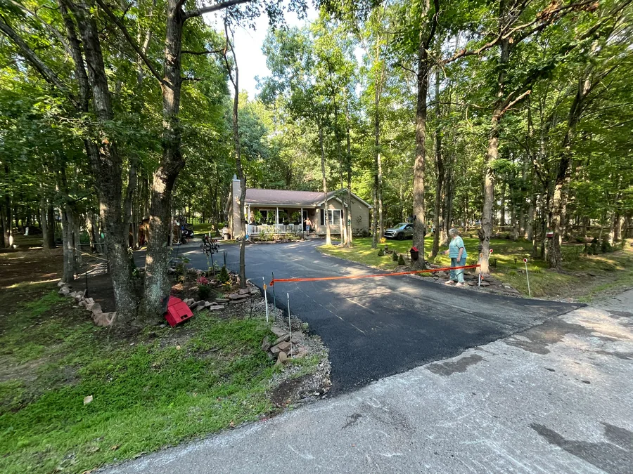 Stone edged garden beds under tall trees beside a fresh driveway, landscape design