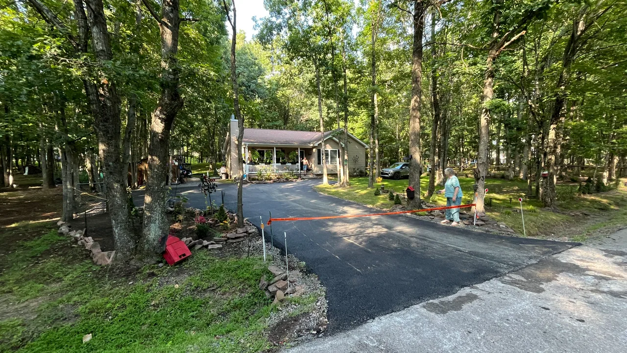 Freshly paved asphalt driveway curving through the woods to a ranch house, asphalt paving