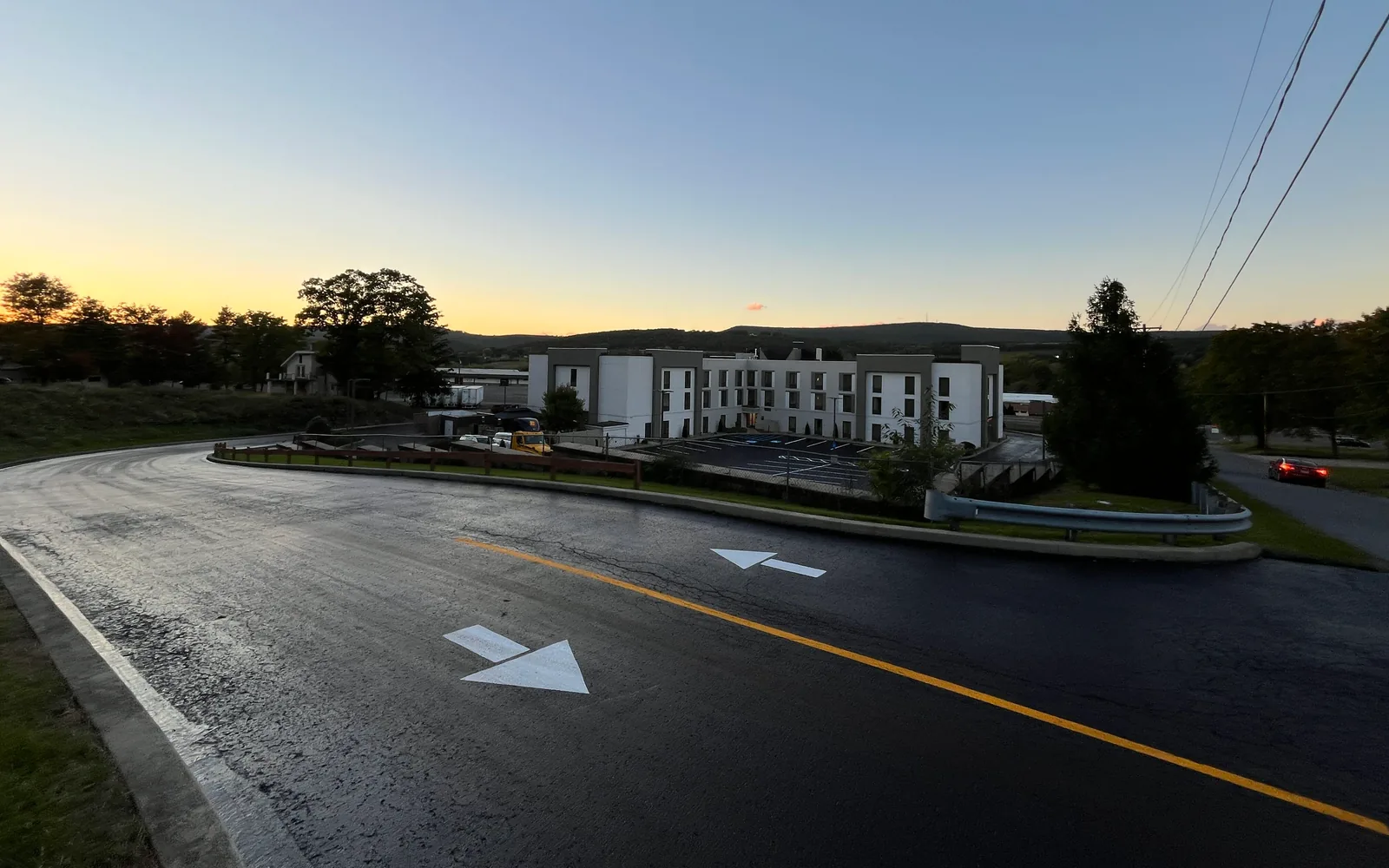 Access drive with a fresh black surface and new arrows above a commercial lot at dusk, parking lot paving