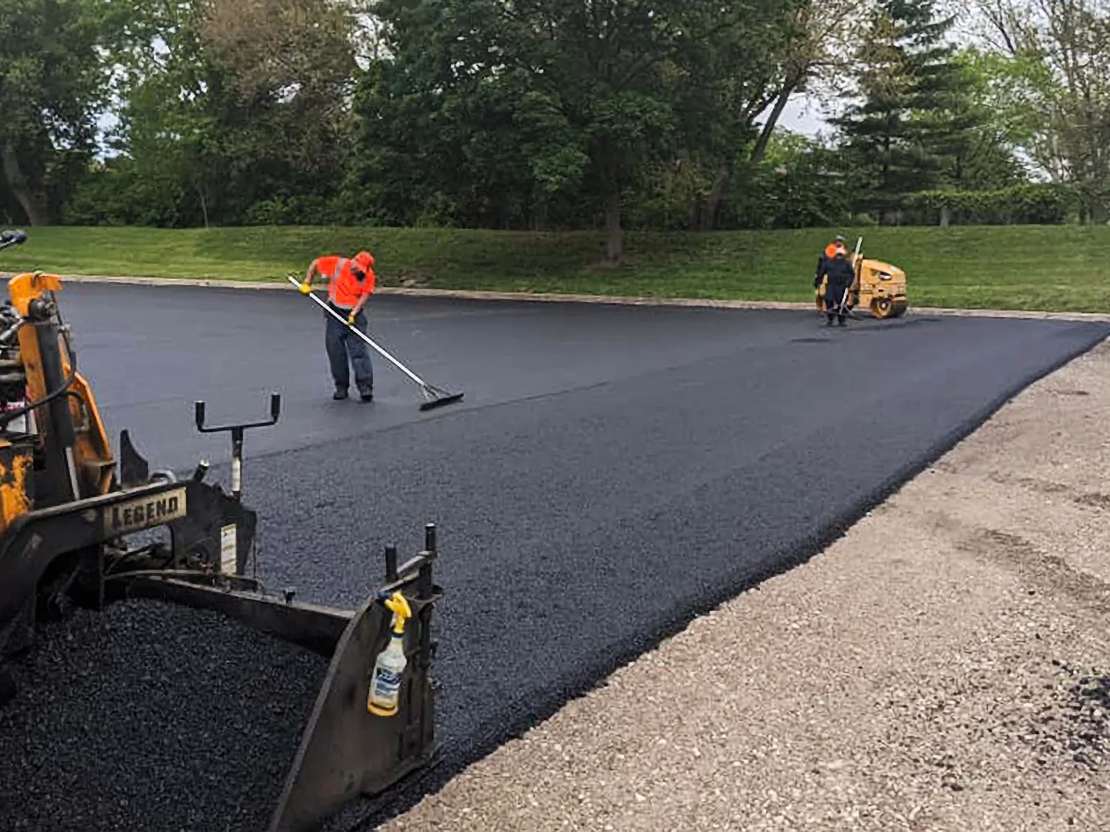 Paver laying new asphalt on a parking lot while a worker rakes the fresh mat, parking lot paving