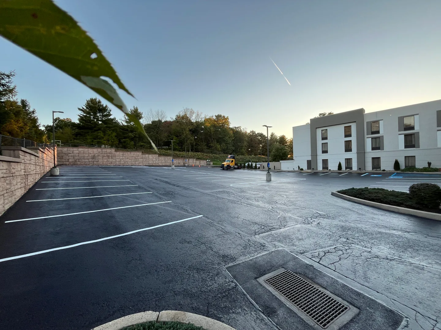 Commercial parking lot with a fresh black surface and new stall lines beside a stone retaining wall, parking lot paving