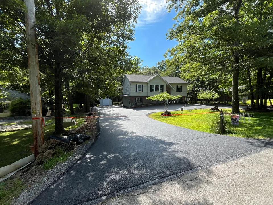 Freshly paved asphalt drive winding through the trees to a raised ranch house, private road paving