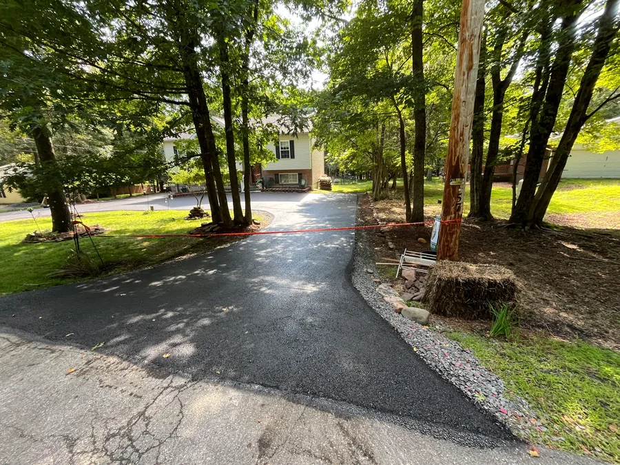 Freshly paved asphalt drive entrance turning into the woods, private road paving