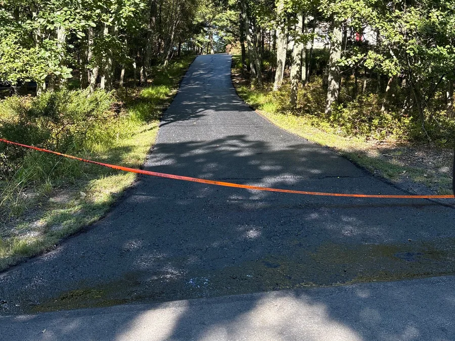 Asphalt private lane climbing through the woods with a tape line across the entrance, private road paving