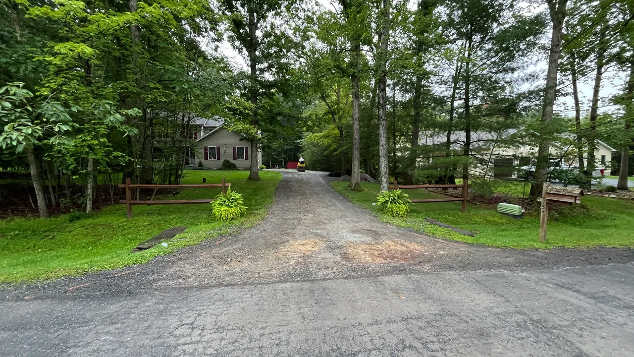 Stone driveway base between split rail fences with a small roller at work, asphalt paving