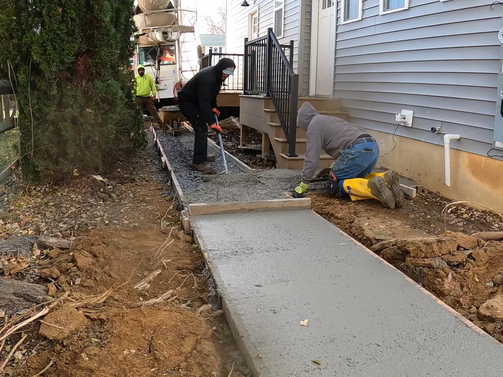 Crew placing and raking a new concrete walkway along a house, walkways and sidewalks